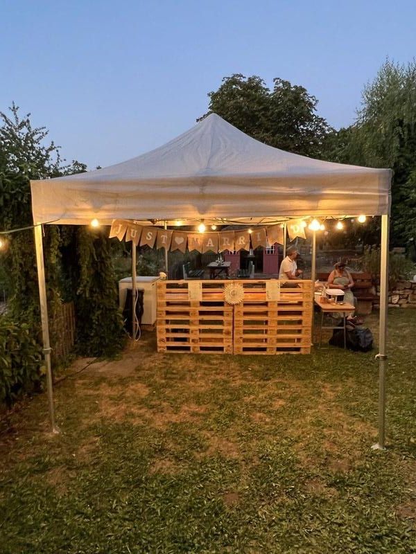 Palettenbar unter Zeltdach mit Lichterketten im Abendlicht